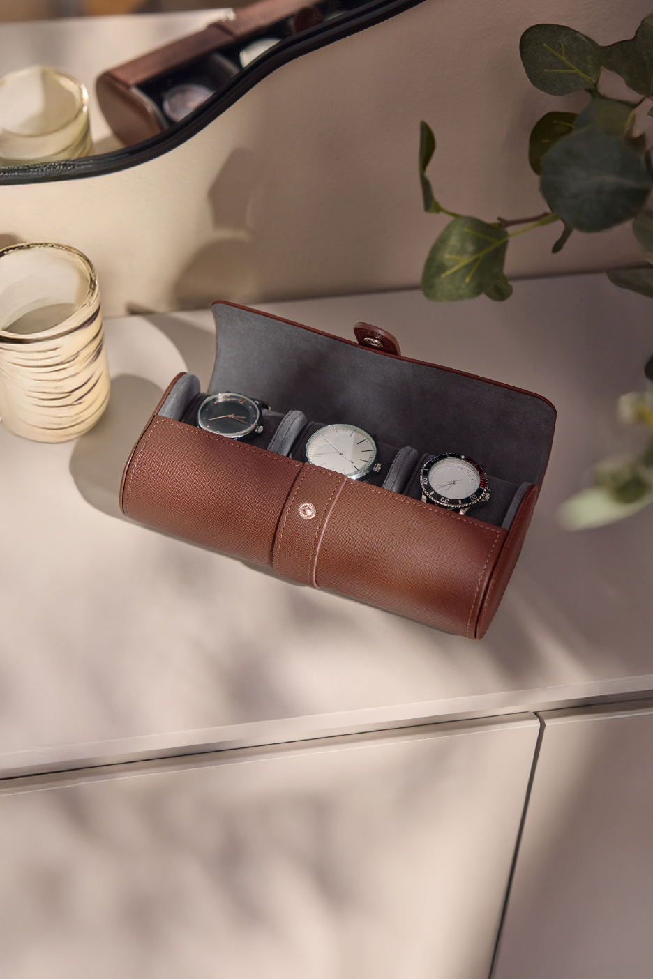 Δερμάτινη θήκη ρολογιών με τρία ρολόγια και μια κούπα σε ένα τραπέζι.